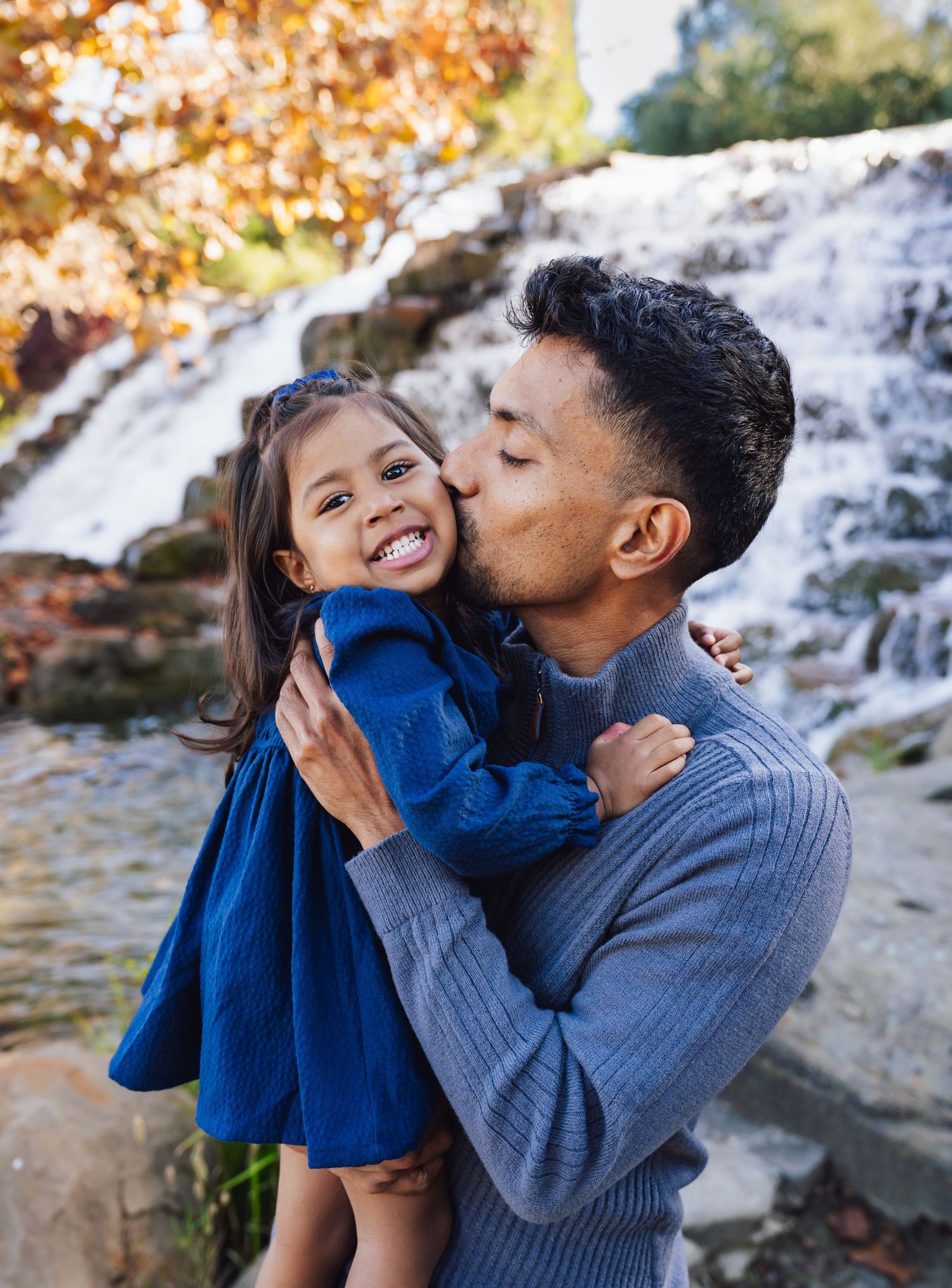 A family sits together on rocks by a waterfall during golden hour on an autumn day.