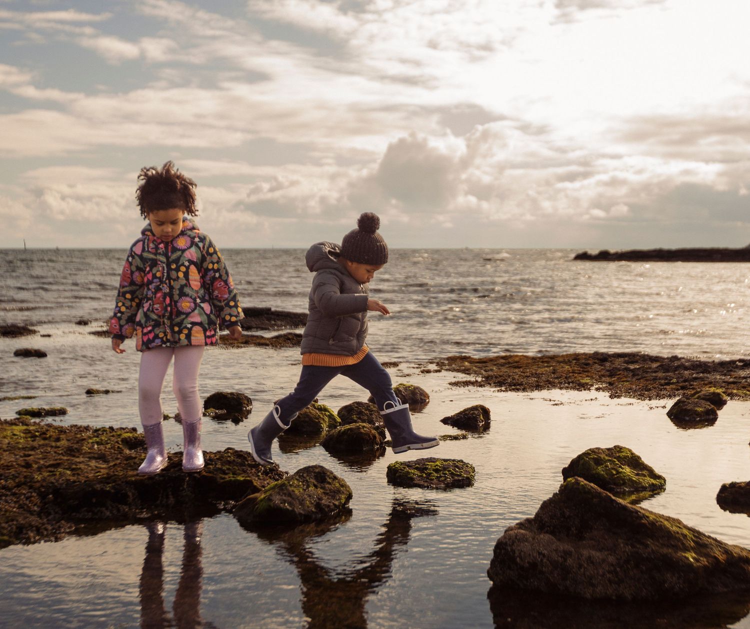 People exploring tide pools along a rocky beach shoreline during golden hour sunset.