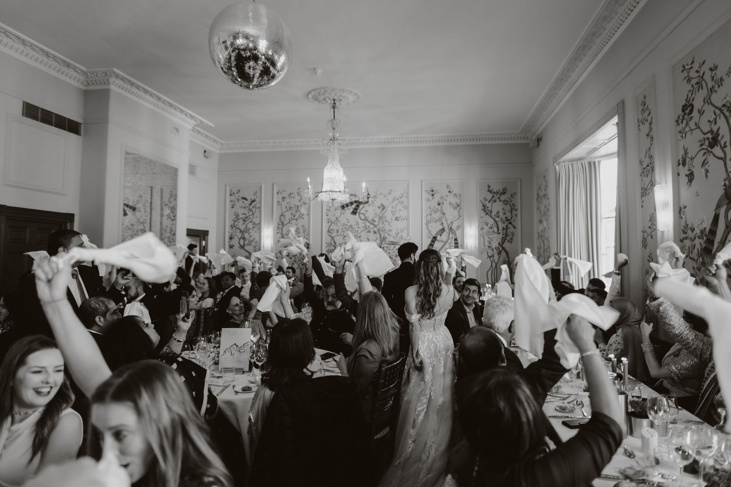 Wedding party in gray and white attire runs playfully across a grassy field at sunset. The George rye