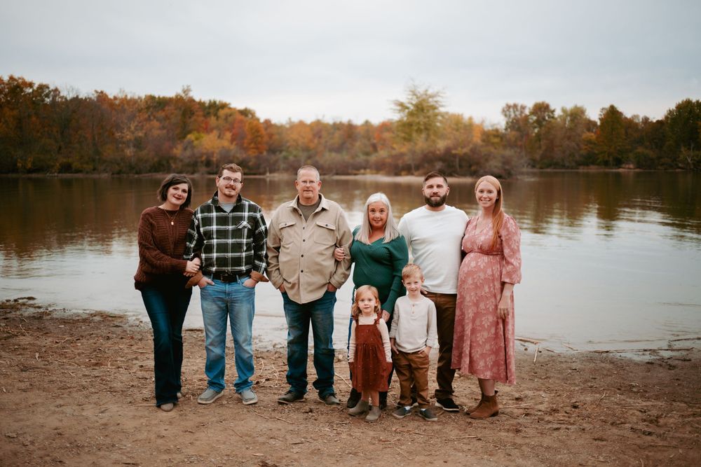 A group of people standing together at sunset by a serene lake with autumn trees in the background.