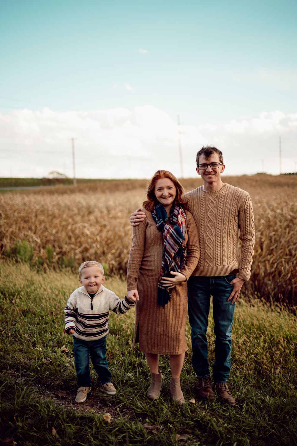 A family stands together in a golden wheat field during sunset creating a warm autumn portrait series.