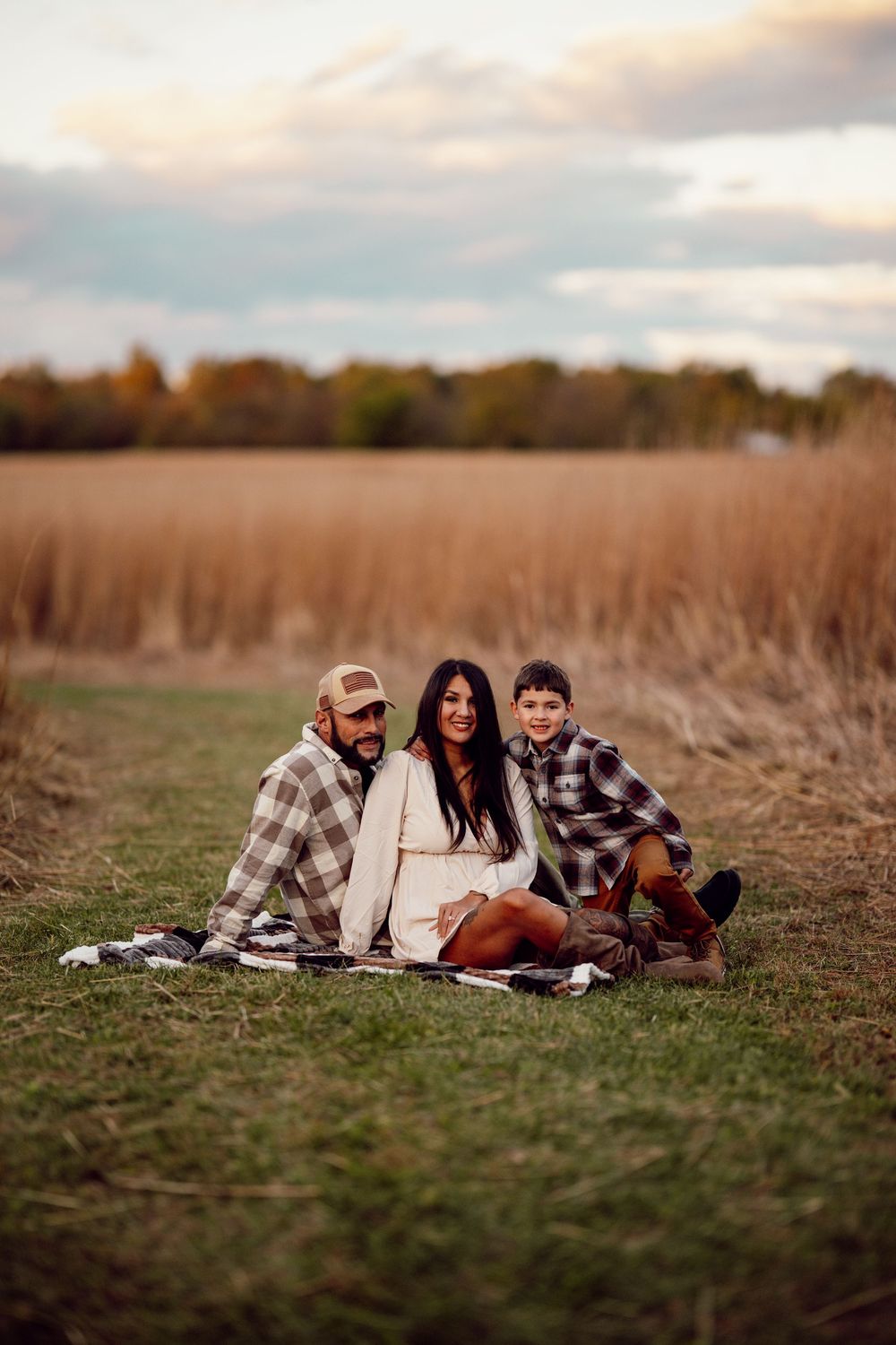 A family relaxes on a blanket in a rustic field during golden hour with tall brown grass in the background.