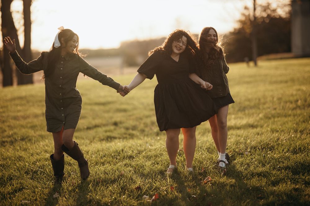 People playing and running together in a grassy field during golden hour sunset.