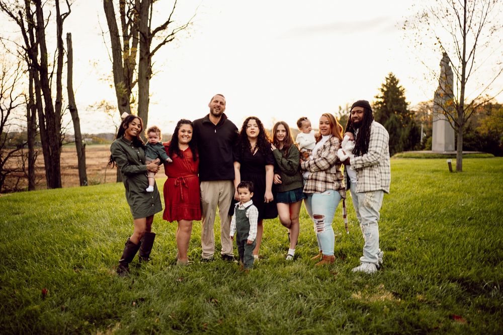 A group of people stand together in a grassy field during autumn, creating a playful line formation.