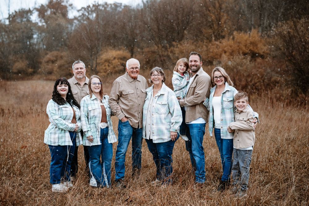 A family poses together in a rustic autumn field wearing coordinating blue and white outfits.