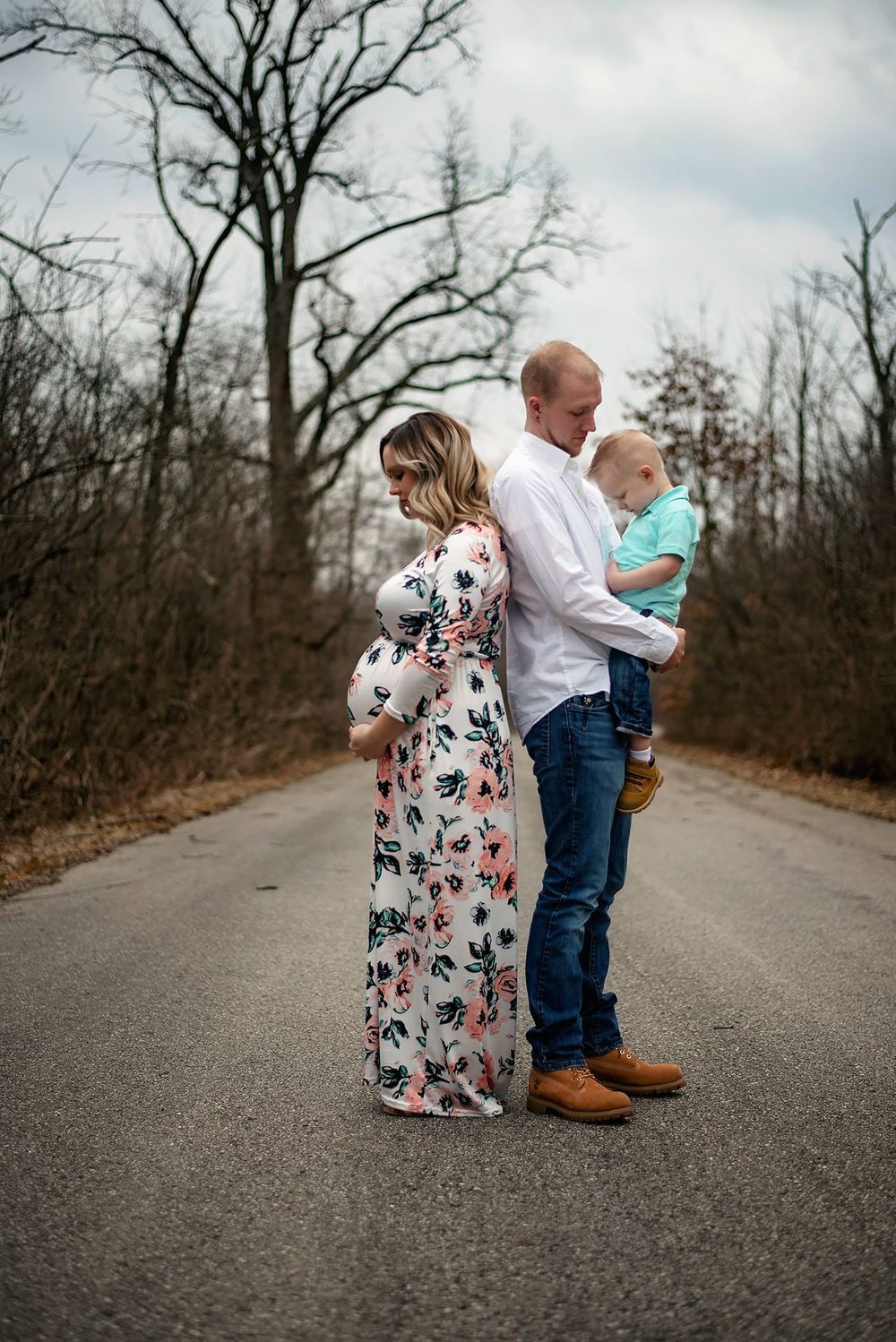 Couple in casual attire standing on an empty road surrounded by bare trees.