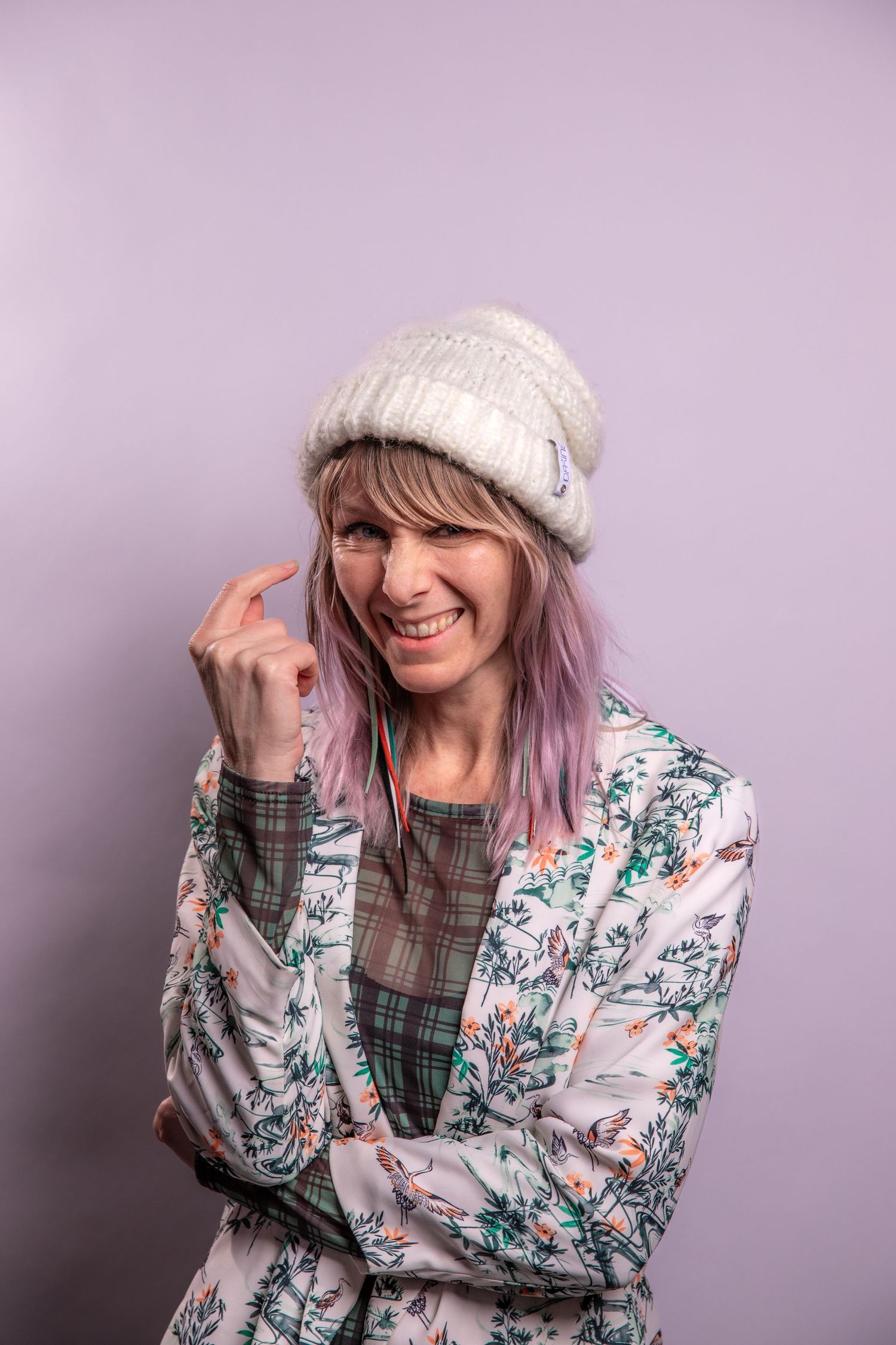 Cozy winter fashion with floral print jacket and knit beanie against purple background.