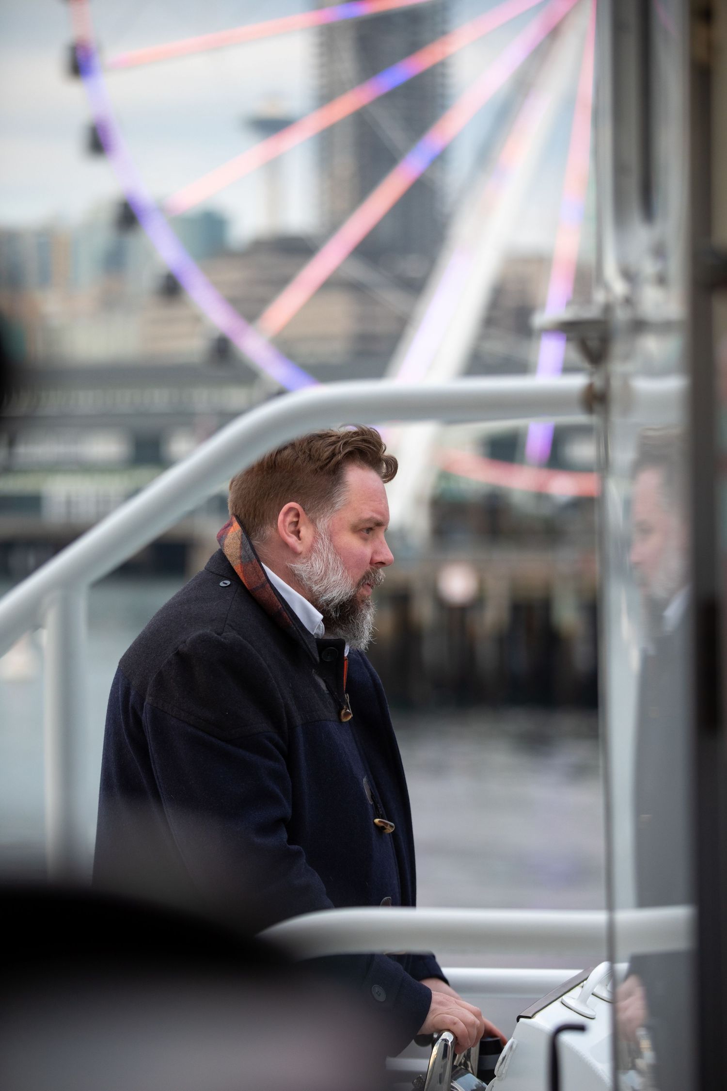 Person in dark coat looking over railing with colorful light streaks in background.