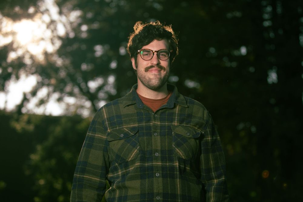 Portrait in warm evening light with a brown plaid shirt against blurred natural background.