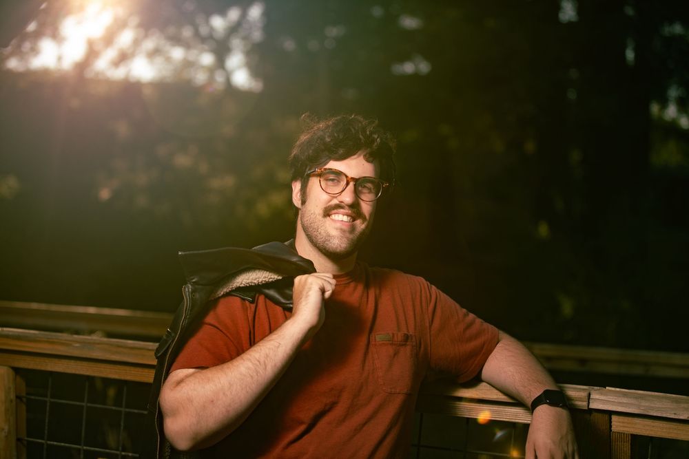 Casual outdoor portrait with wooden bench and natural lighting during golden hour.