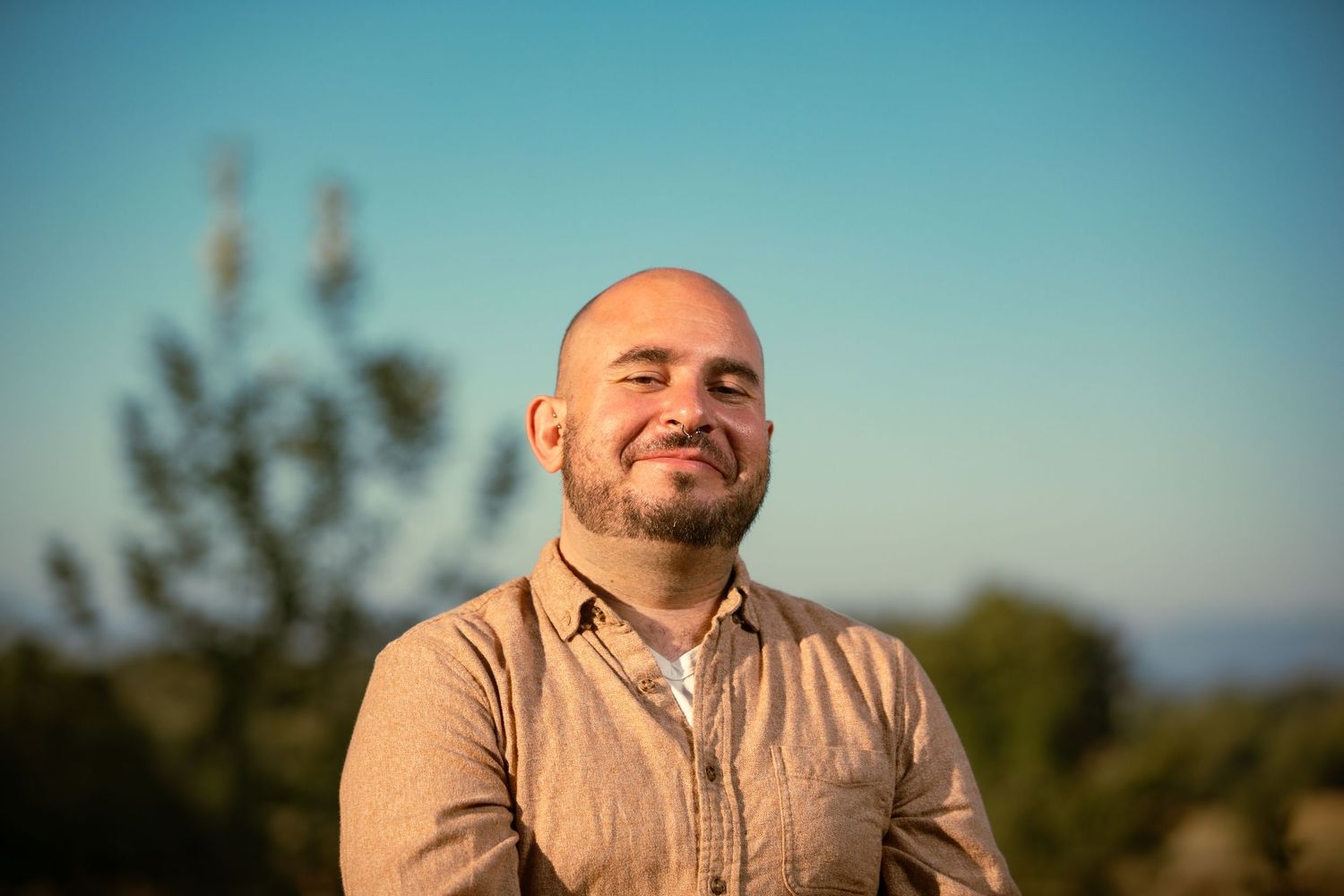 Person in light colored shirt sitting outdoors against bright blue sky background.