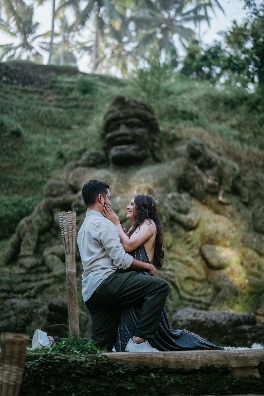 A romantic couple shares an intimate moment on a rustic wooden bench surrounded by lush tropical foliage.