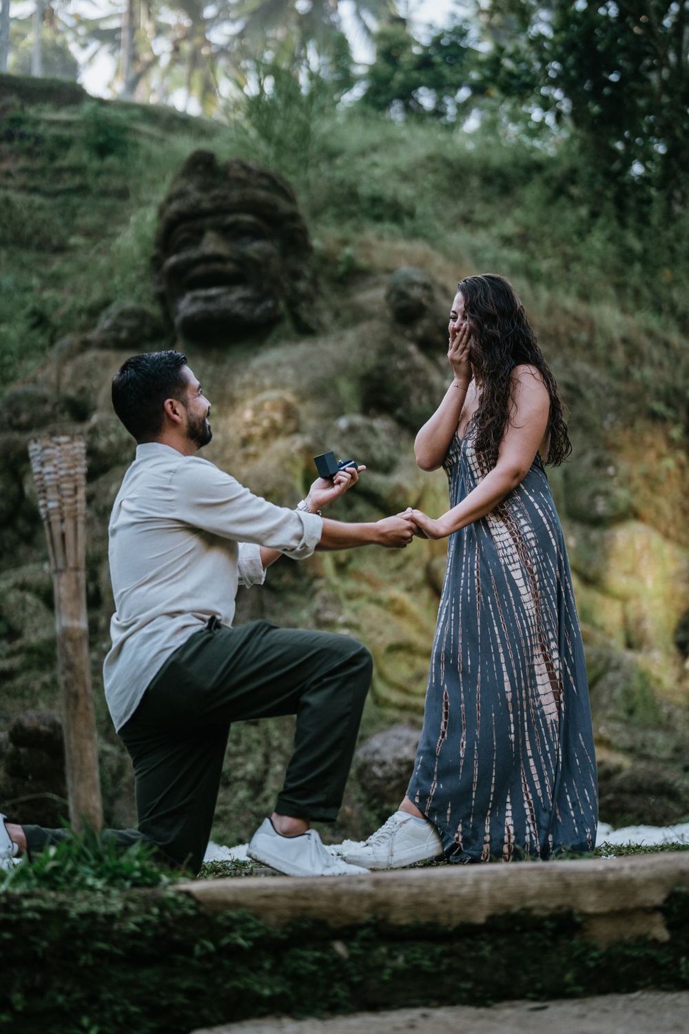 A couple shares a playful moment on a wooden bench in a tropical garden setting.