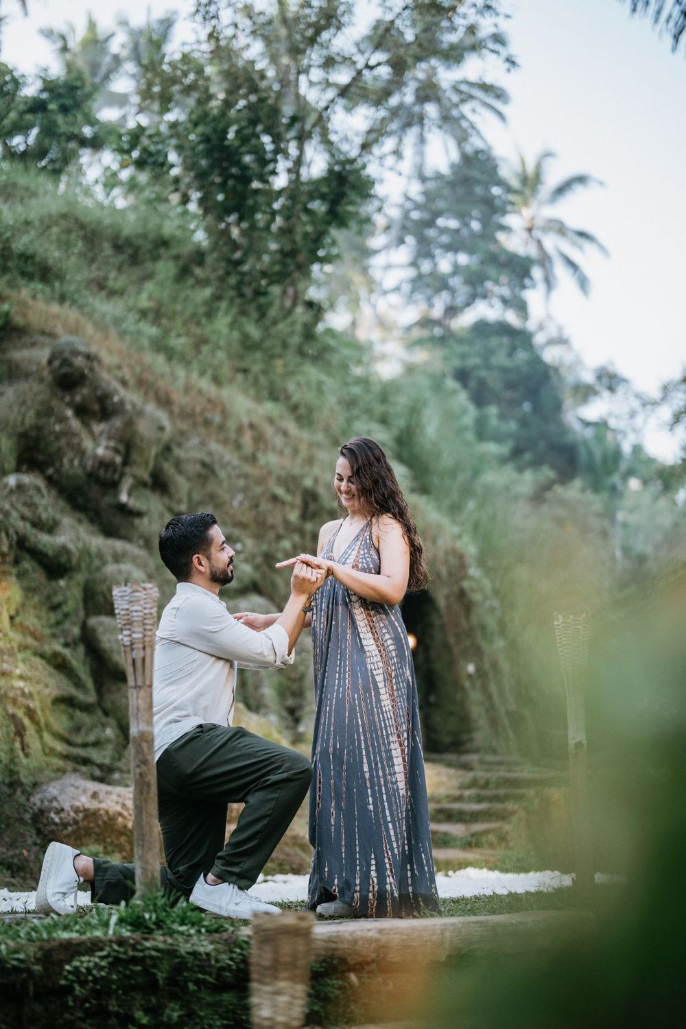 A couple engages in conversation while sitting on a rustic bench amidst tropical greenery.