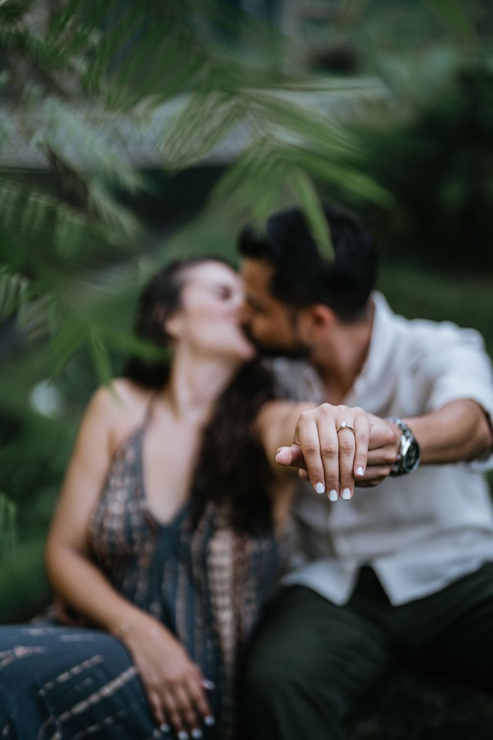 Close-up shot of an engagement ring as a couple shares an intimate moment in a tropical setting.