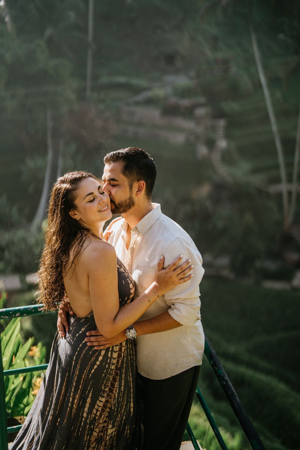 A couple shares an intimate moment in golden sunlight against a backdrop of tropical foliage.