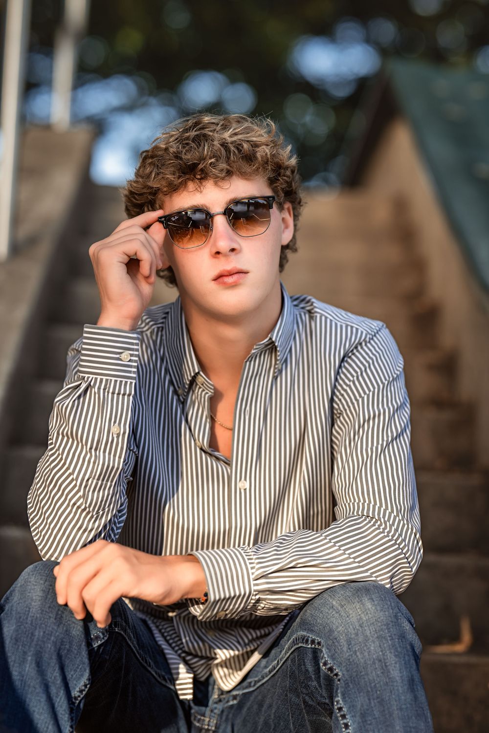A casual lifestyle portrait of a high school senior boy wearing sunglasses and a striped shirt while relaxing outdoors.