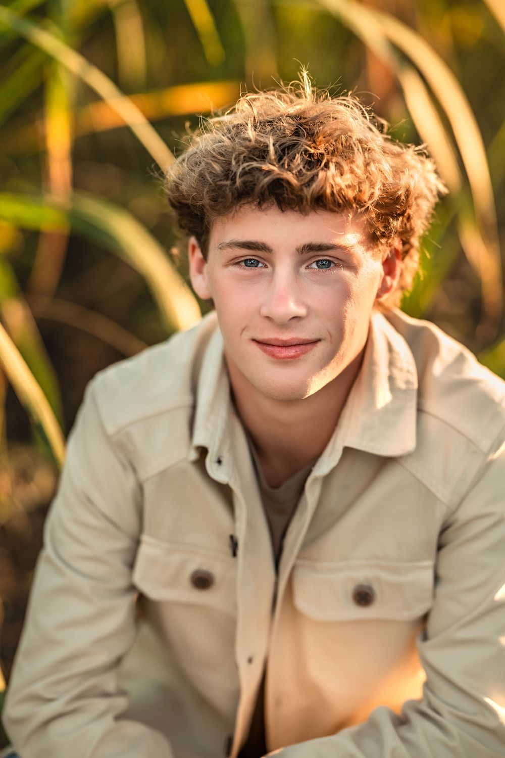 Warm sunlit portrait of a senior boy wearing a beige jacket against a natural blurred background.