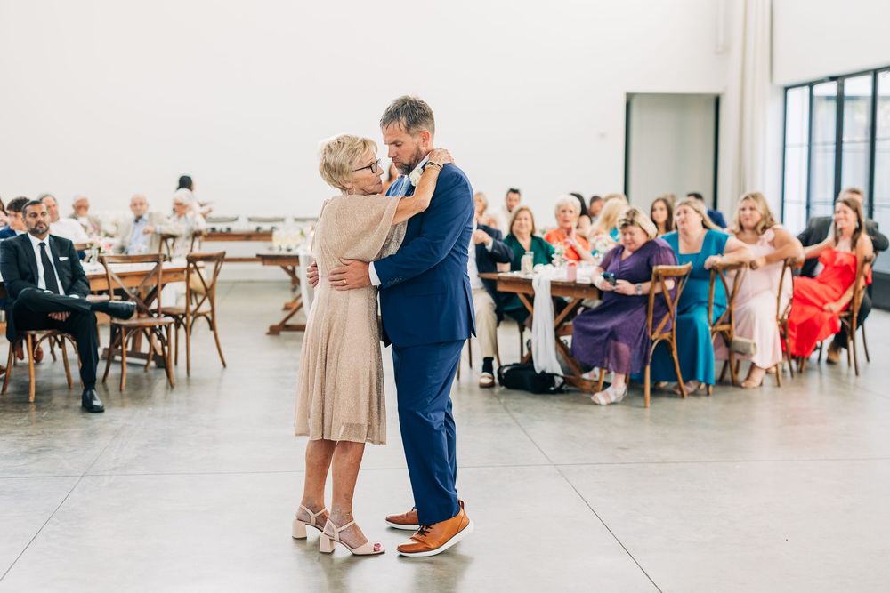 Couples dance together on a white wooden floor during a reception celebration in a bright indoor venue.