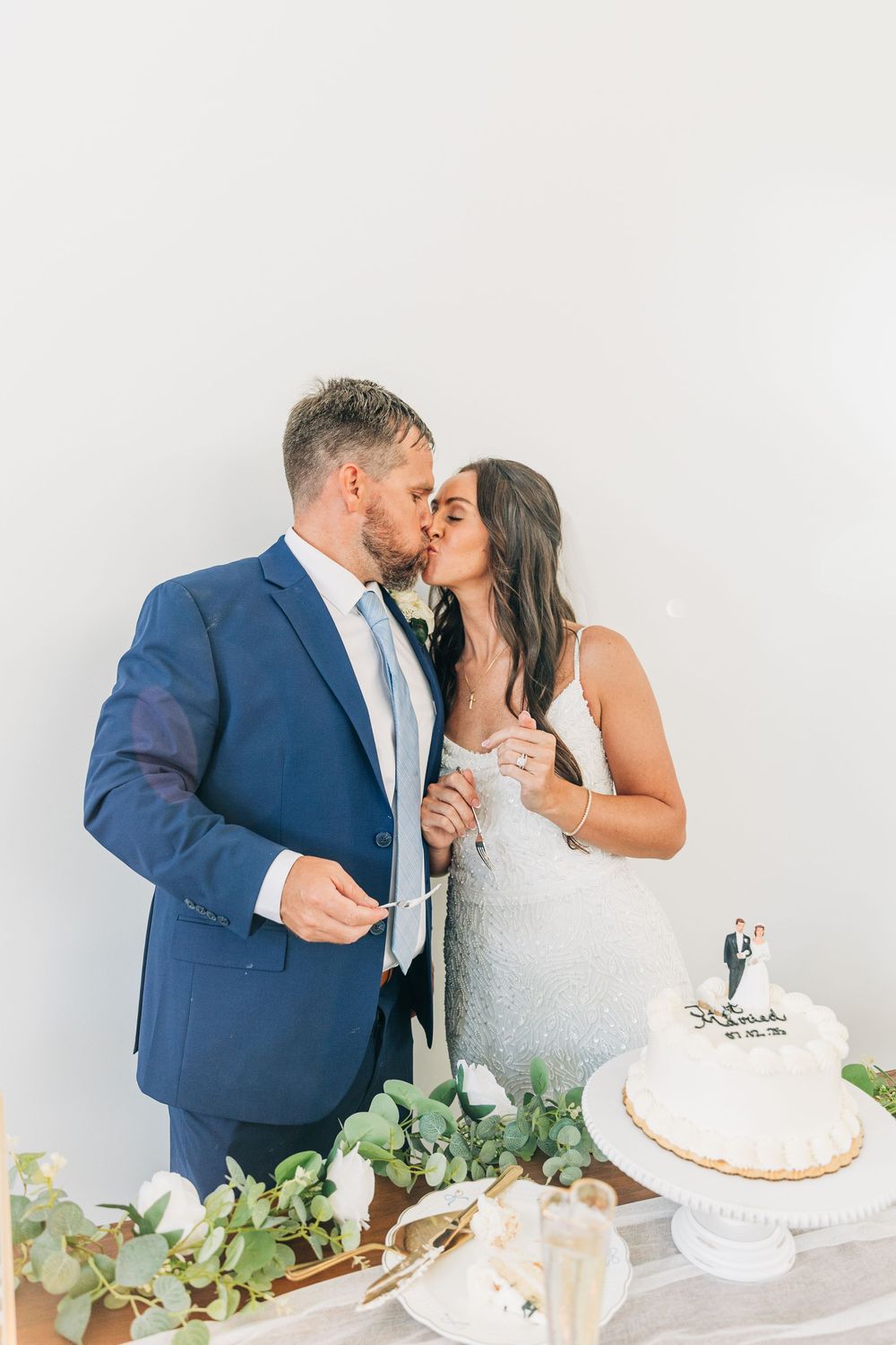 Romantic moment between bride in white dress and groom in navy suit while cutting their wedding cake.