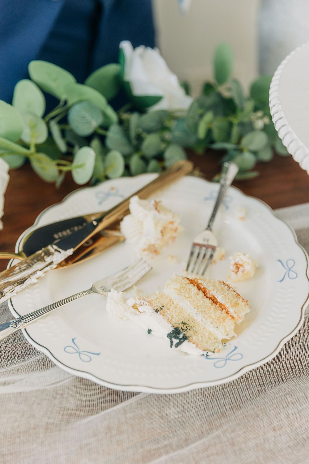 Half-eaten slices of wedding cake on white plates with forks and eucalyptus garland decor.