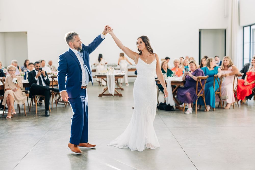 Dancing couple leads a joyful reception celebration while guests cheer and clap in a bright modern venue.