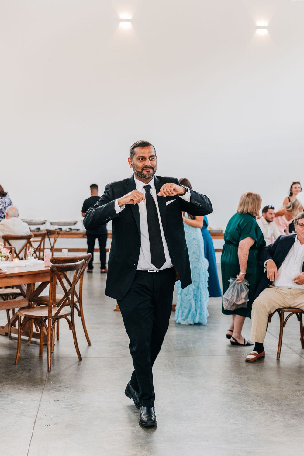 A series of dance moves by a man in a black suit performing during a wedding reception on a polished concrete floor.
