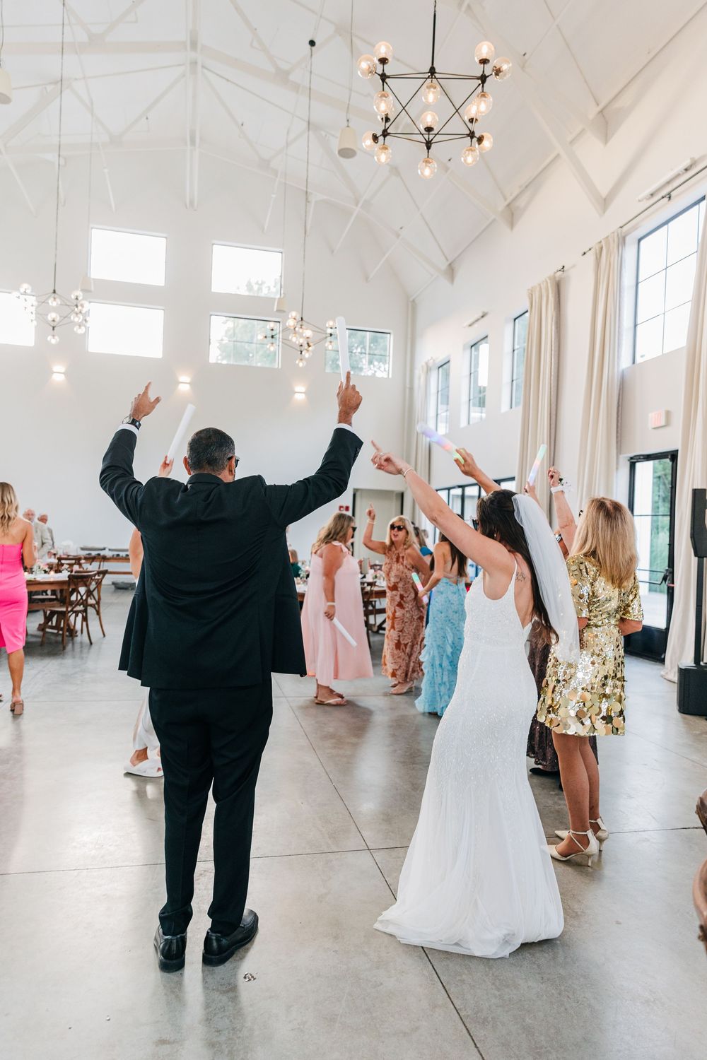 Wedding celebration in a bright white reception hall with guests dancing and interacting.