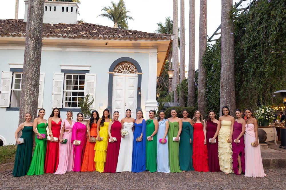 Wedding party bridesmaids lined up wearing colorful rainbow dresses against white church building exterior.