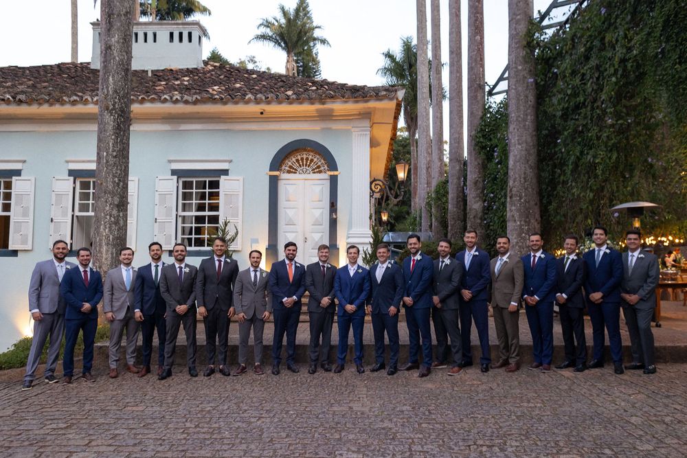 Groomsmen in formal attire stand in a row by palm trees at a wedding venue.