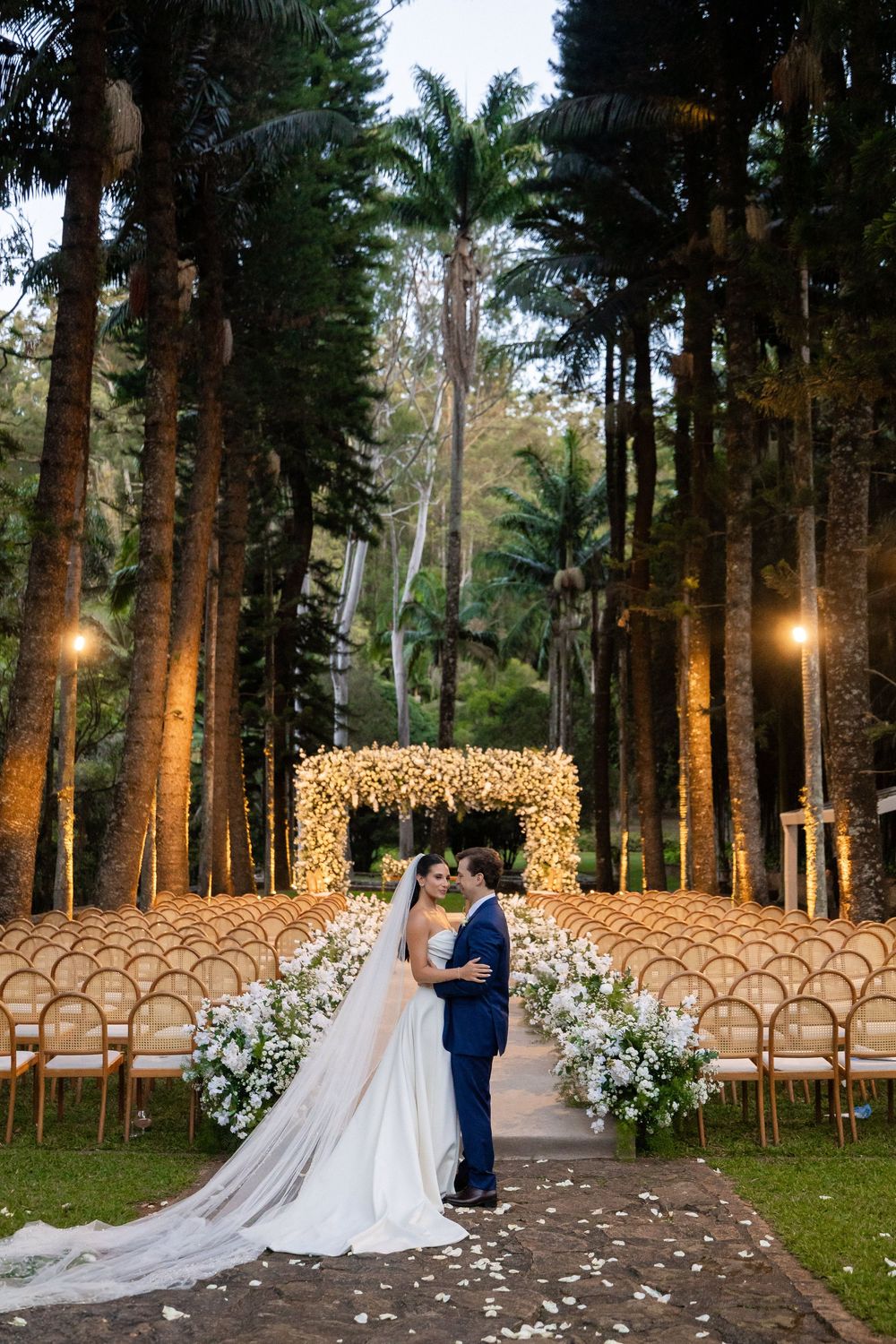 Romantic outdoor wedding ceremony setup in pine forest with fairy lights and wooden chairs arranged in rows.