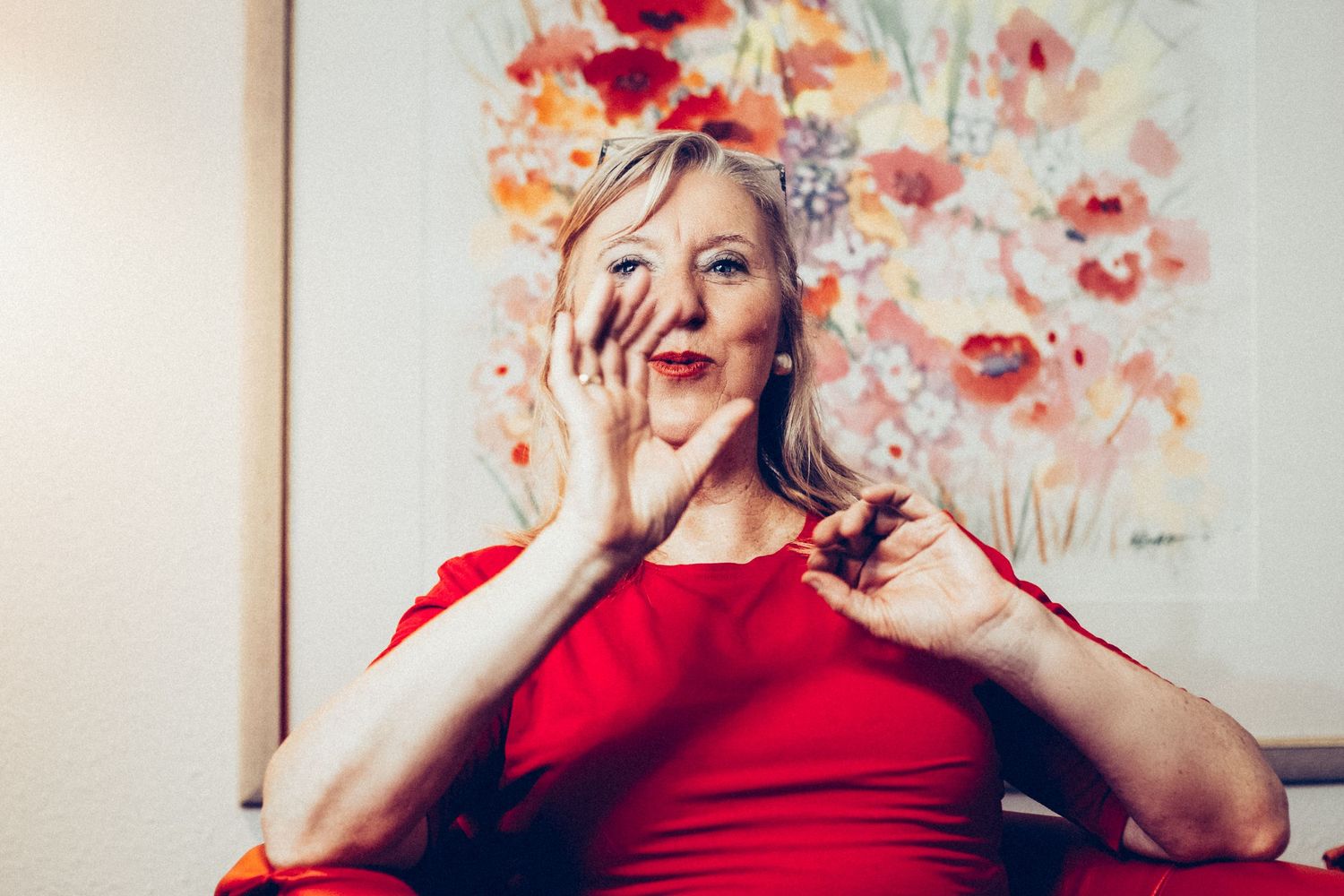 A person in a vibrant red dress laughs joyfully against a backdrop of colorful floral artwork.