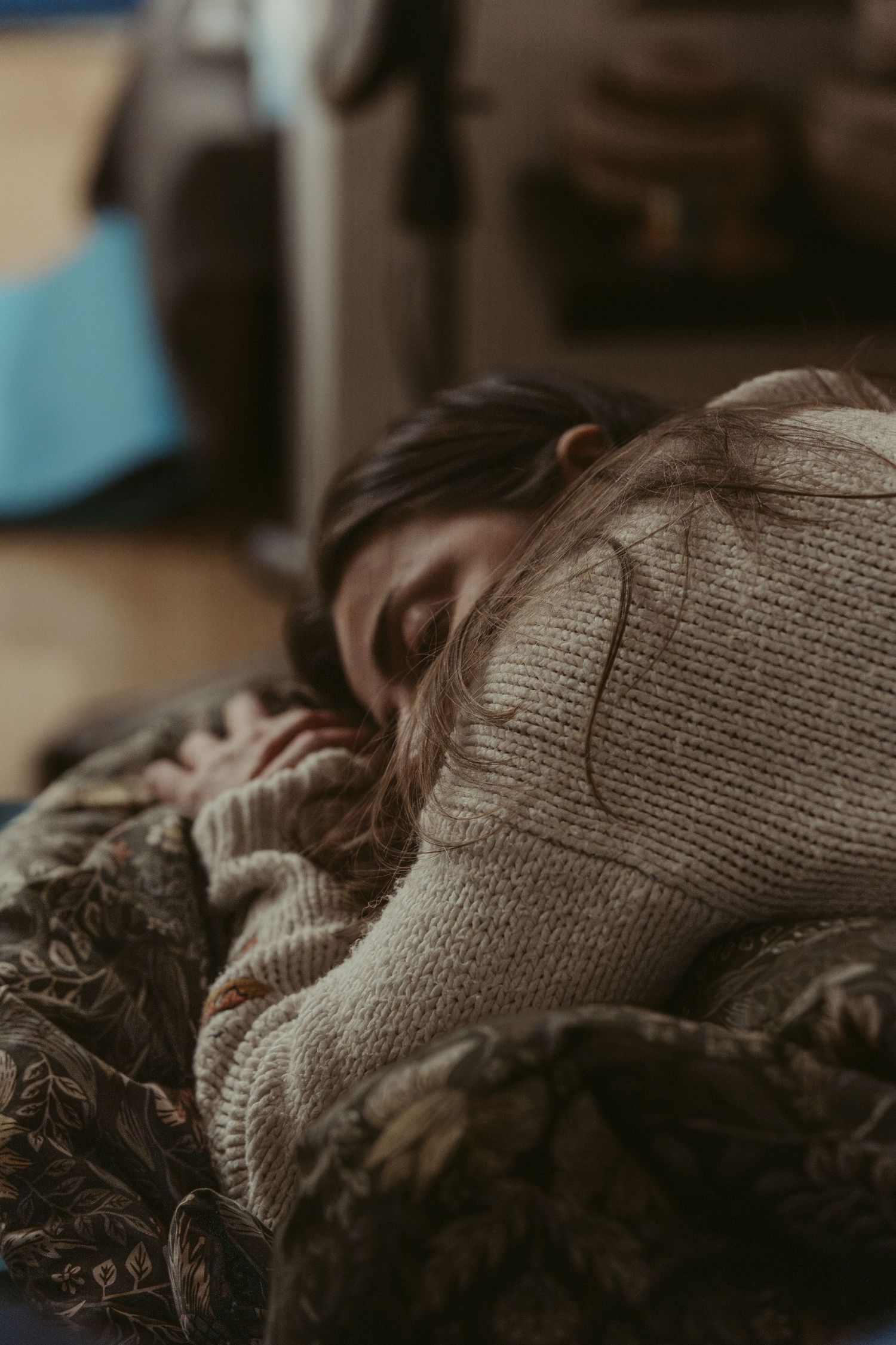 Someone rests peacefully under cozy blankets wearing a warm knit sweater in soft, moody lighting. Home birth in Iceland photography.