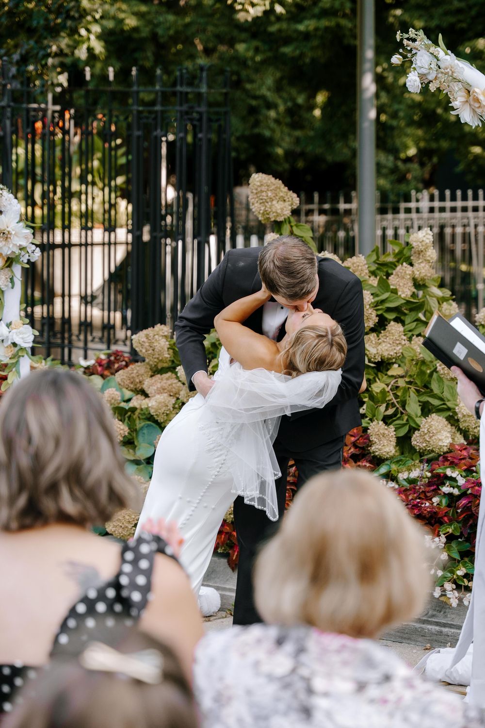 A series of four photos showing a traditional wedding dip pose in front of a garden fence with white flowers.