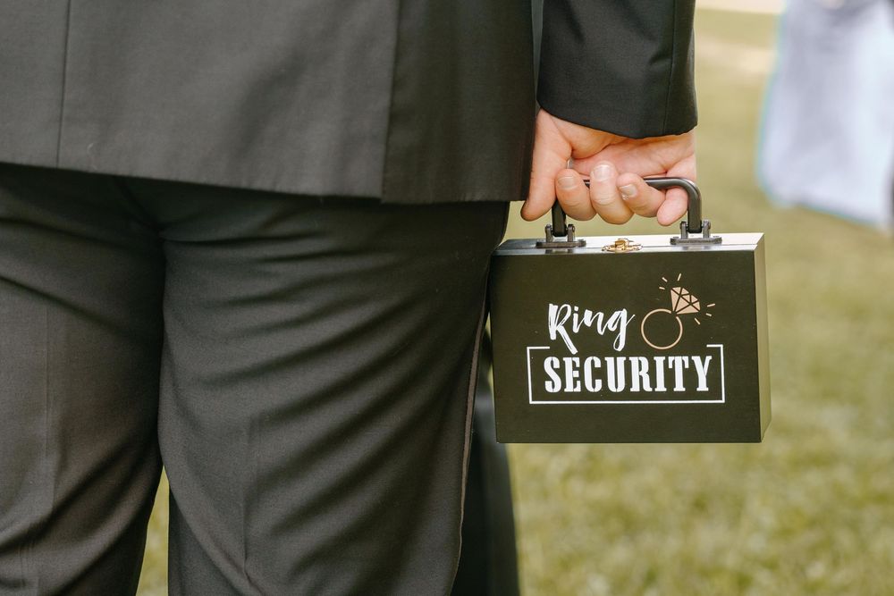 Wedding guests wearing formal tuxedos enjoy a festive reception outdoors while a security guard stands watch.