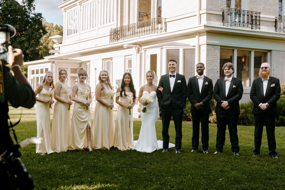 Elegant wedding party lined up in front of a white historic mansion with columns.