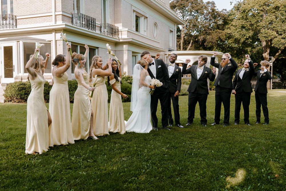 Wedding party stands in line across a sunny lawn during an outdoor celebration at an elegant venue.