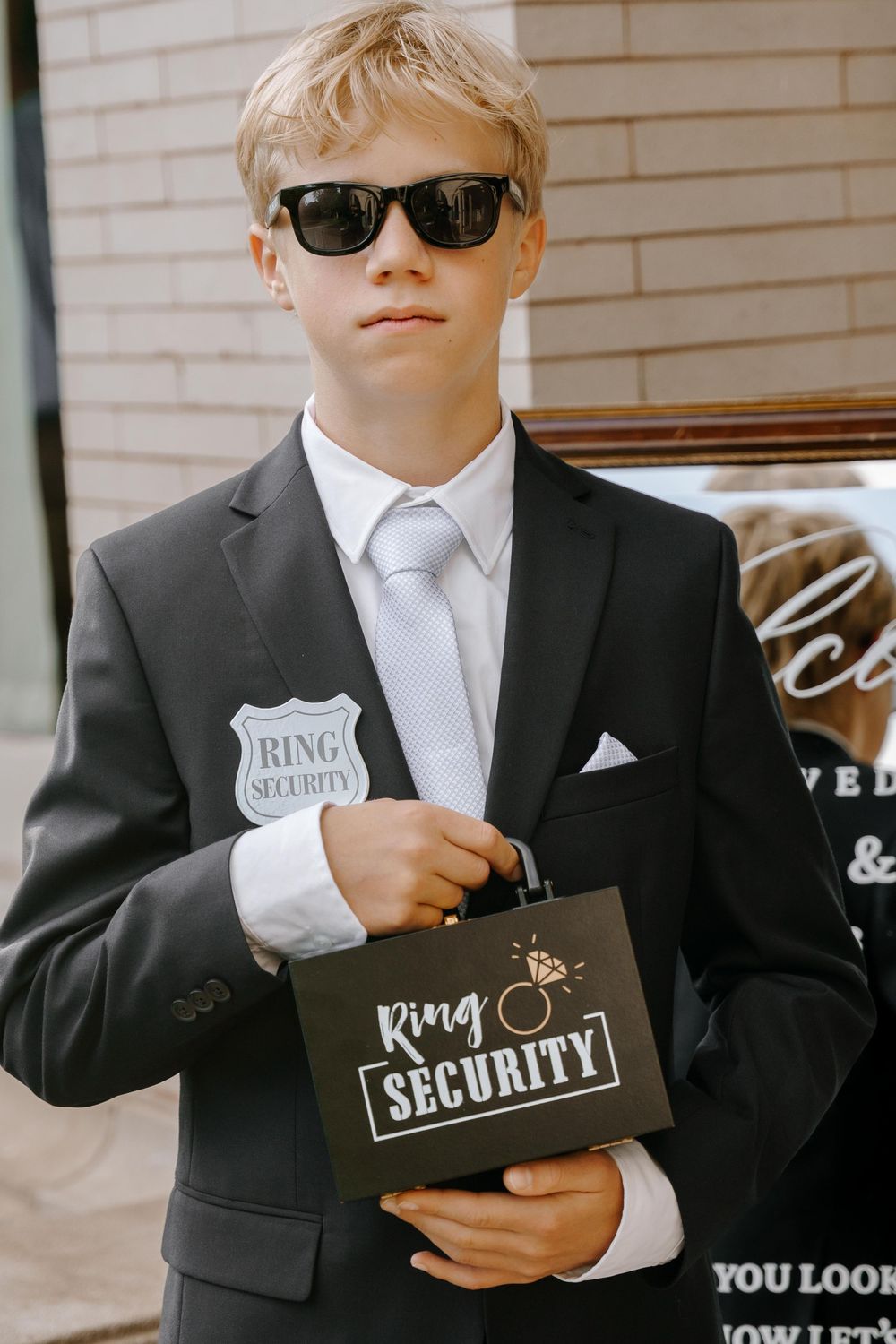 Young ring bearers in formal suits hold small black gift boxes at a wedding.