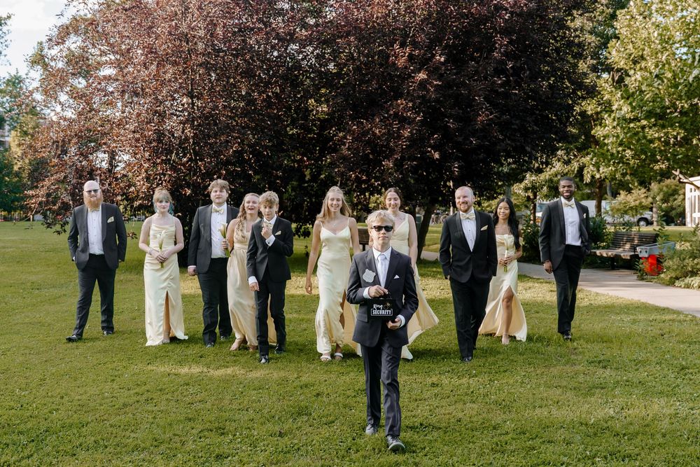 Wedding party poses together on a lush green lawn with autumn trees creating a scenic backdrop.