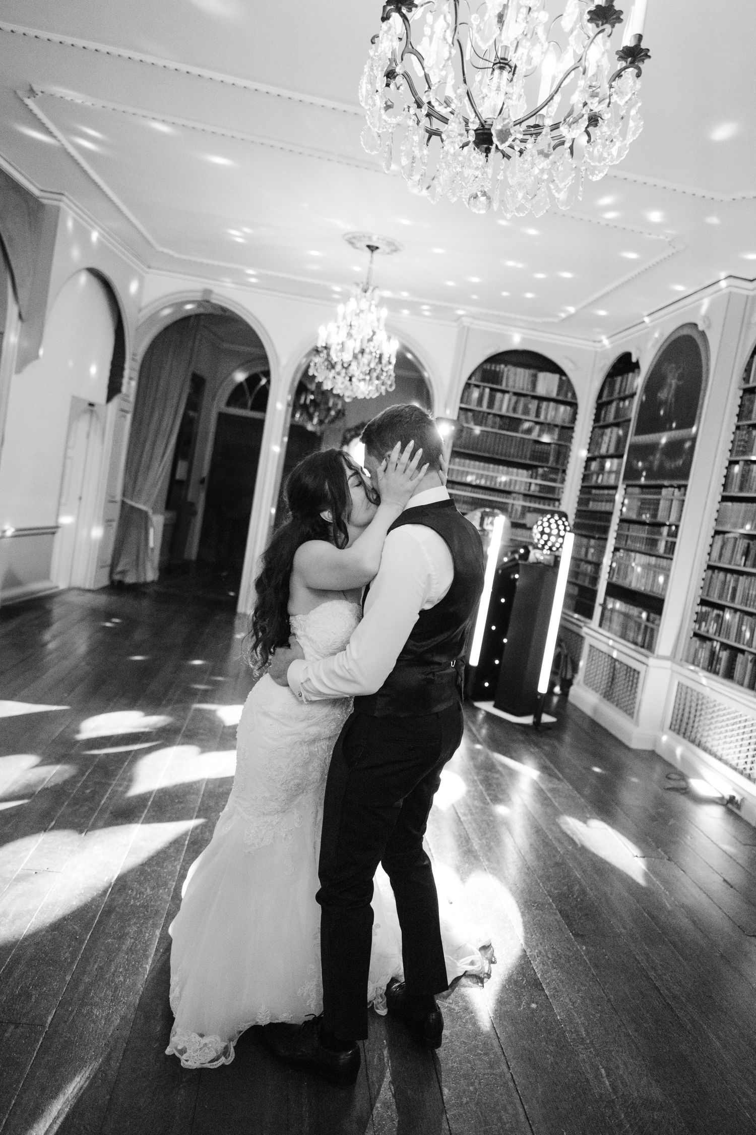 A romantic first dance between newlyweds in an elegant ballroom with crystal chandeliers and dark hardwood floors.