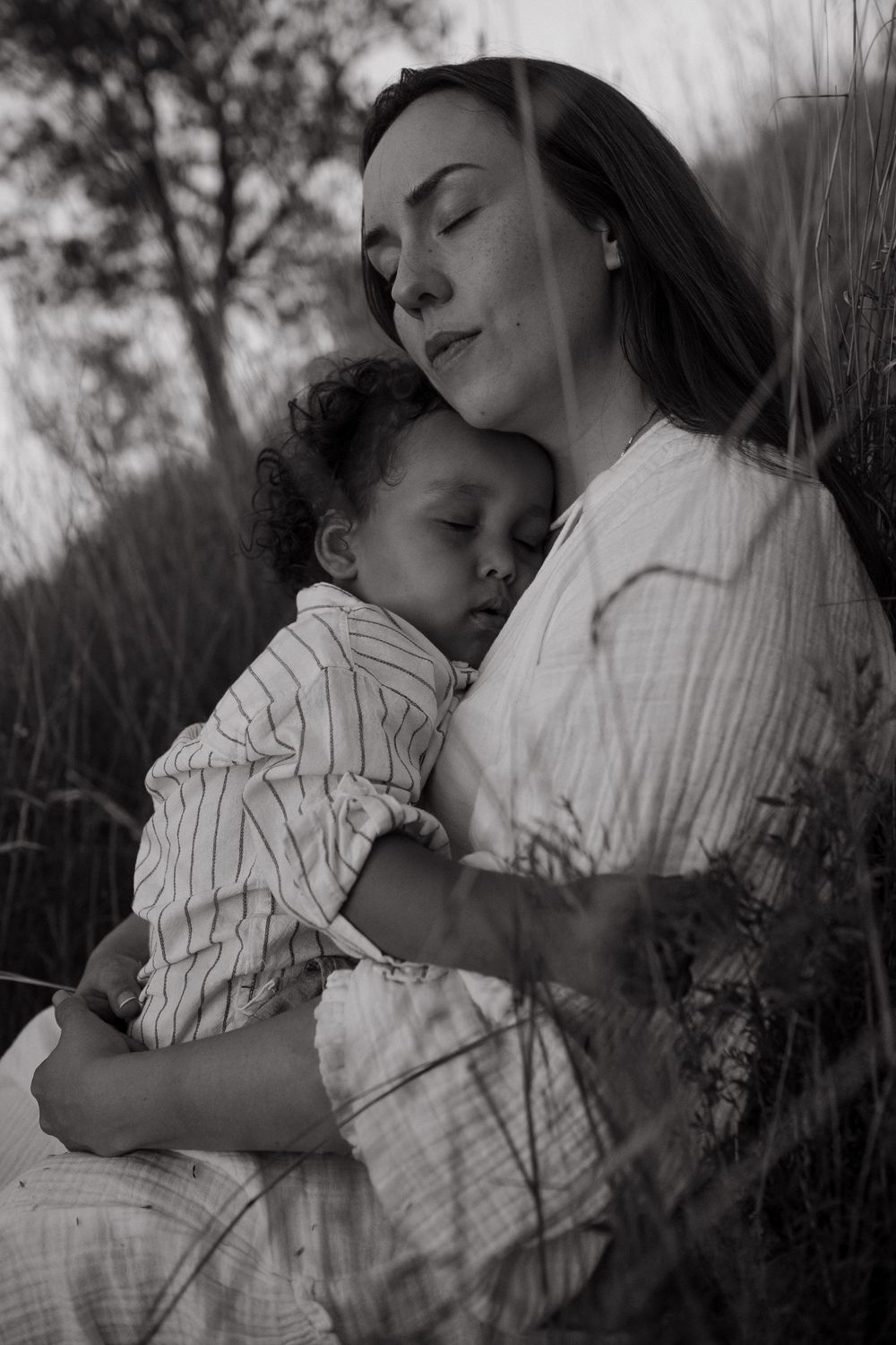 mom and son sitting in a field with closed eyes while being captured by candid family photographer in Stockholm