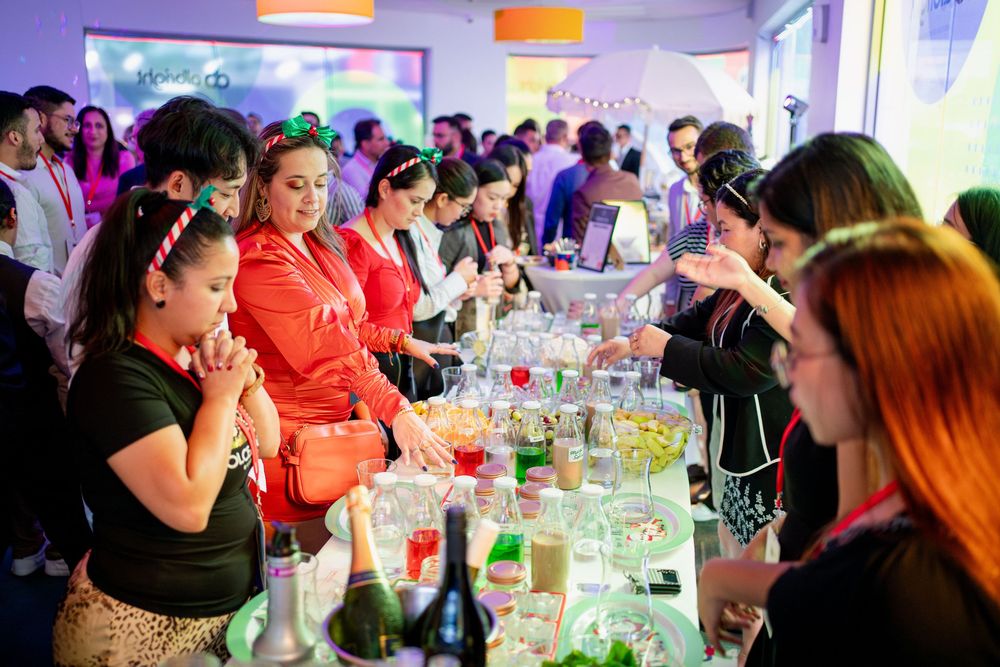 Event space filled with attendees seated at long tables with colorful mood lighting overhead.