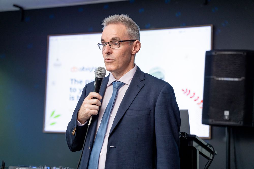 Professional speaker presenting at a business conference with dark background and stage lighting.