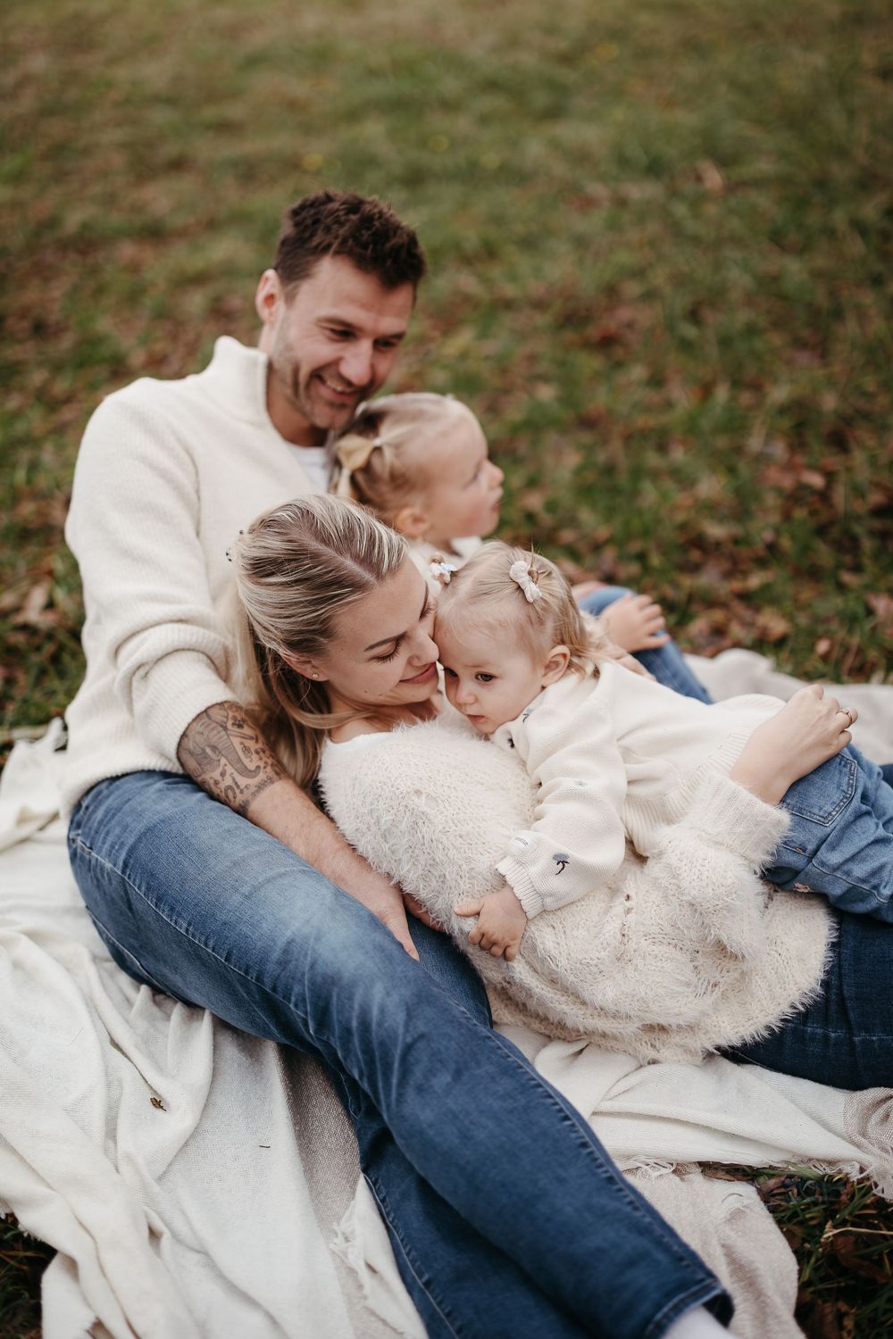 Smiling father and mother cuddle their two little girls on a grassy lawn during an autumn family photo session.