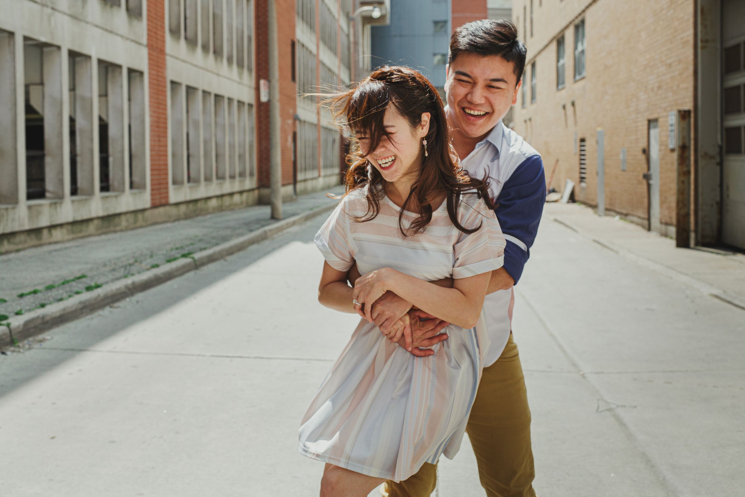 A couple shares romantic moments while walking along a bright urban street with stone buildings.
