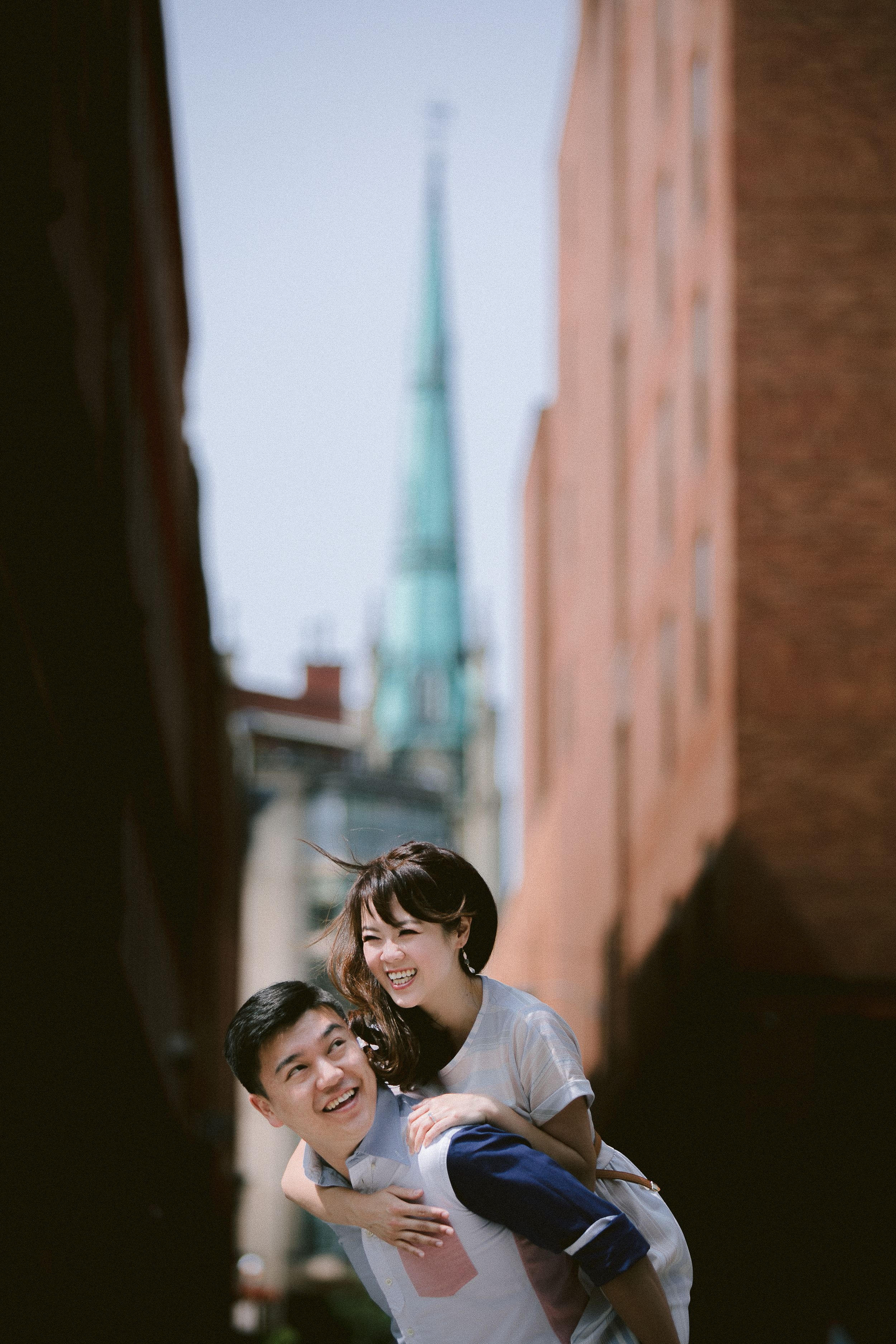 A romantic couple shares intimate moments while walking through a European city street with church spires visible.