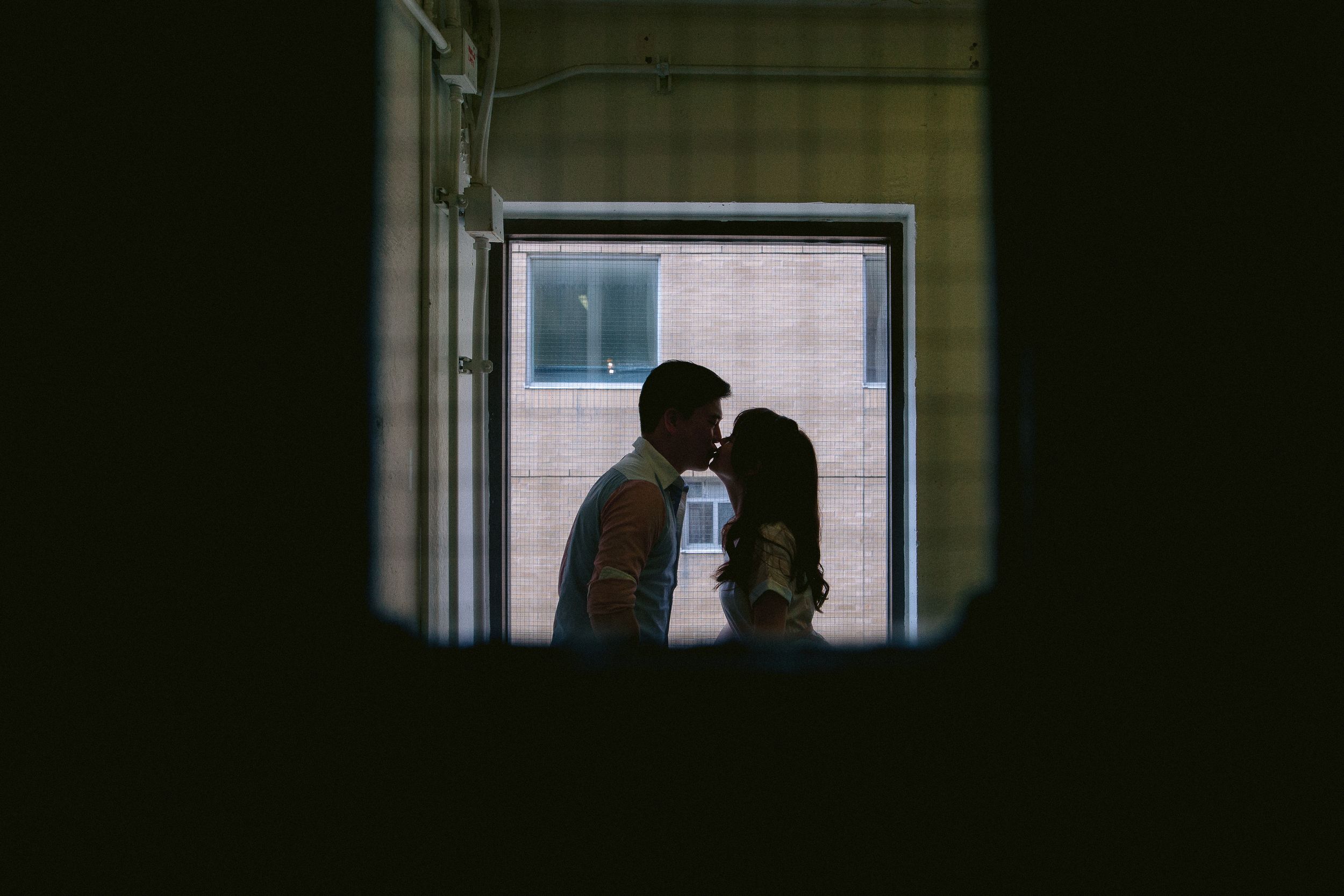 Two figures share an intimate silhouetted moment against a dark interior window backdrop.