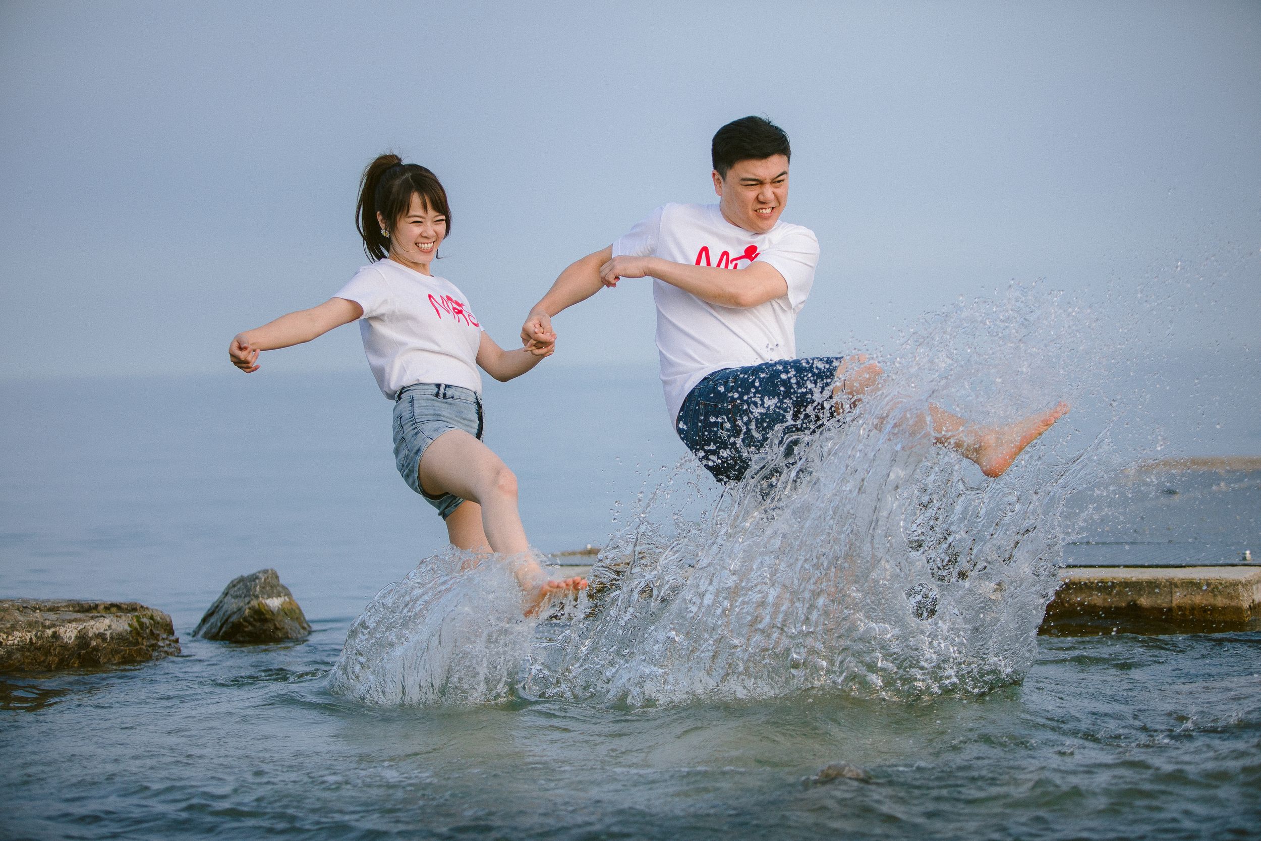 A couple splashes and plays together in shallow ocean water wearing coordinated outfits.