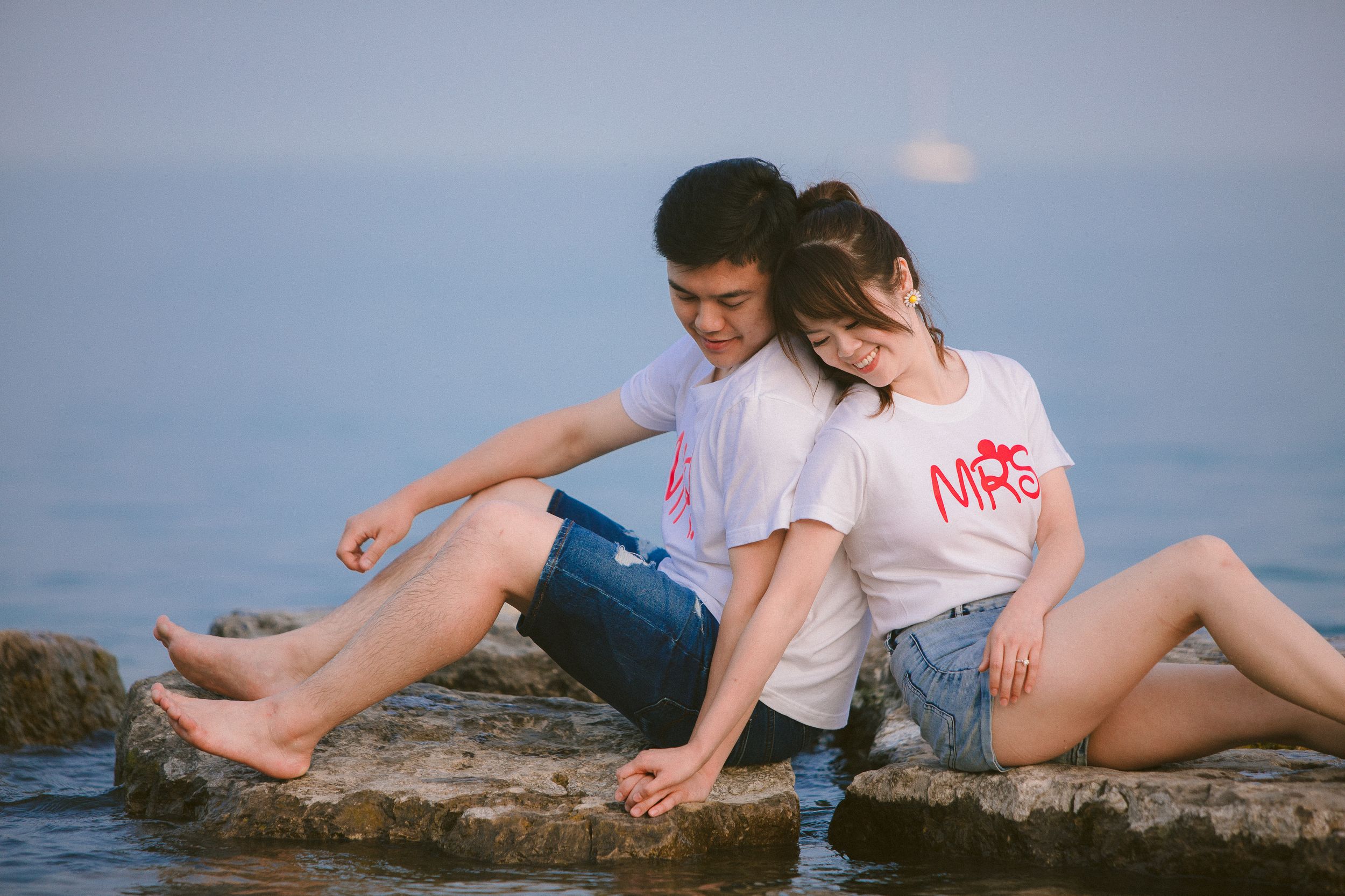 A couple shares an intimate moment on a red wooden bench at the beach.