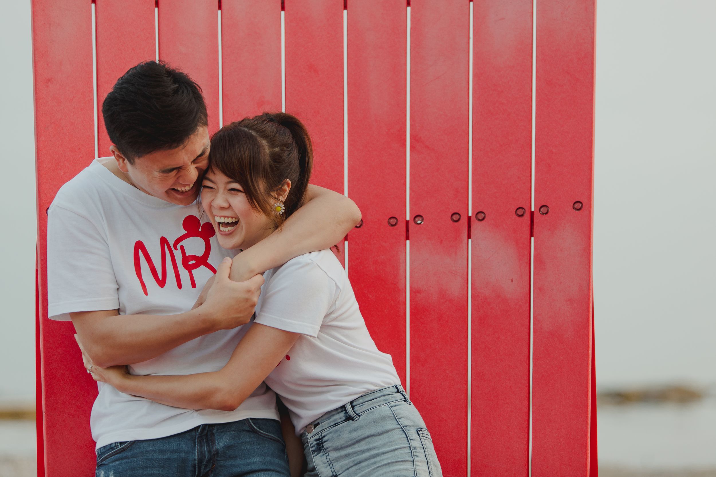Two people share a joyful moment while sitting close together on a red beach bench.